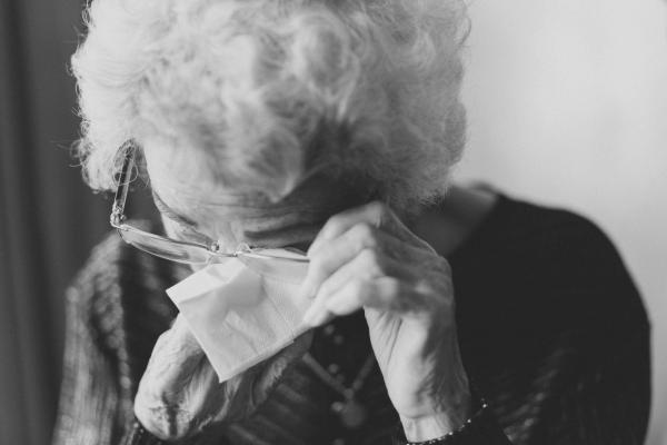 An image in black and white of an elderly woman wiping her eyes with a tissue