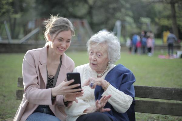elderly woman sat on a bench with a younger woman looking at a mobile phone together