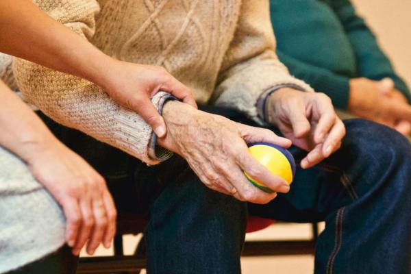 A person holding the wrist of an elderly patient while sat down next to each other.