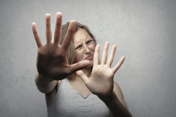 A woman holding her hands up to the camera with a pained expression on her face.